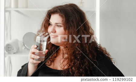 Water diet. Weight loss hydration. Body positive. Relaxed satisfied overweight obese woman with glass in light interior with free space. 119299102