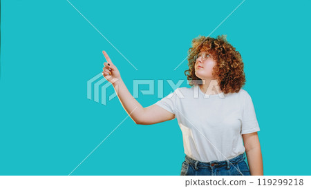 Advertising people. Smart curious woman pointing finger upwards isolated on blue copy space background. Advertising people. Smart curious woman pointing finger upwards isolated on blue copy space background. 119299218