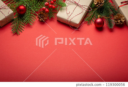 Christmas or New Year celebration red paper festive background with decoration fir tree, wrapped present boxes, cones, berries, sparkly red balls. Space for text. 119300056