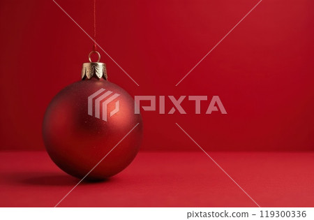 A vibrant red Christmas ornament ball is hanging gracefully from a string against a rich red background, creating a festive atmosphere A vibrant red Christmas ornament ball is hanging gracefully from a string against a rich red background, creating a festive atmosphere 119300336