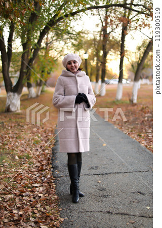 Woman in a light autumn coat against the background of fallen withered leaves Woman in a light autumn coat against the background of fallen withered leaves 119300519
