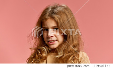 Girl's half-smile suggests playful hesitation, her eyes hinting at mischief against soft pink studio background. 119301152