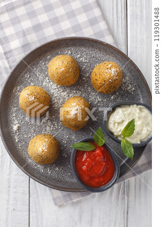 Arancini are Italian rice balls that are stuffed with cheese and pepper served with two sauces close-up in a plate. Vertical top view 119301488