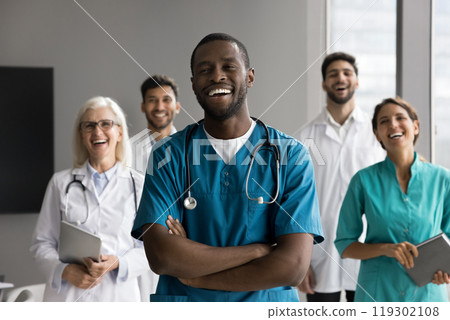 Laughing young Black male surgeon stand before multicultural medics group 119302108