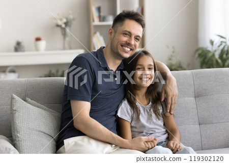 Smiling dad relax on couch hugging beloved little daughter dreaming 119302120