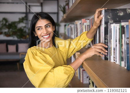 Cheerful young Indian student girl enjoying reading hobby 119302121