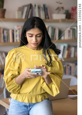 Serious engaged young Indian student woman typing on smartphone Serious engaged young Indian student woman typing on smartphone 119302148