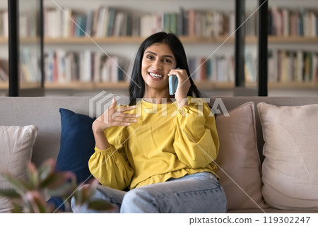 Positive young Indian woman talking on mobile phone on couch Positive young Indian woman talking on mobile phone on couch 119302247