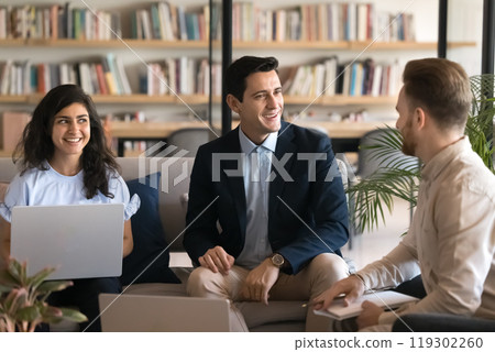 Positive confident young Latin businessman talking to colleagues in co-working Positive confident young Latin businessman talking to colleagues in co-working 119302260