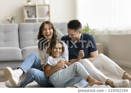 Laughing millennial spouses with preteen daughter playing tickling on floor Laughing millennial spouses with preteen daughter playing tickling on floor 119302284