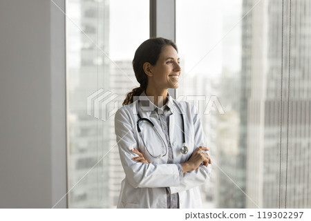 Happy young lady physician stand by window look at distance 119302297