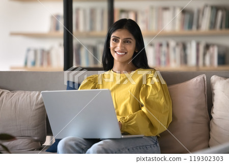 Happy young Indian student girl working on project at laptop 119302303