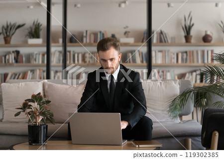 Serious young businessman in suit and tie working at laptop 119302385
