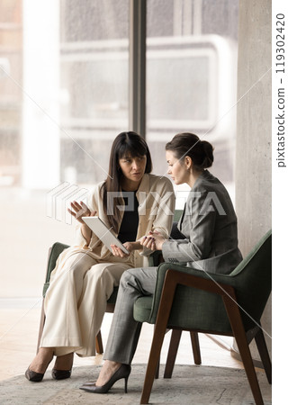 Two business women meeting, talking in office lounge Two business women meeting, talking in office lounge 119302420