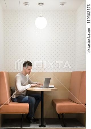 Focused freelancer man working at laptop in office booth Focused freelancer man working at laptop in office booth 119302578