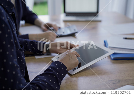 Accountants or auditors reviewing financial documents while sitting at the wooden desk in office. Professionals are analyzing paper reports using tablet computer, close up. Audit and taxes 119302701