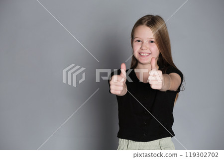 A girl gives two thumbs up with a beaming smile, a gesture of approval. Captures the positivity and enthusiasm of youth. A girl gives two thumbs up with a beaming smile, a gesture of approval. Captures the positivity and enthusiasm of youth. 119302702