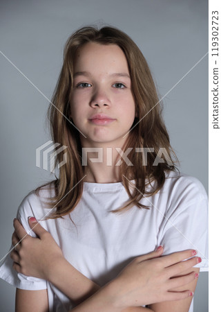 A young girl in a white t shirt crosses her arms and looks directly at the camera with a calm expression. This image highlights the confidence and self-assurance of youth in a modern context. A young girl in a white t shirt crosses her arms and looks directly at the camera with a calm expression. This image highlights the confidence and self-assurance of youth in a modern context. 119302723