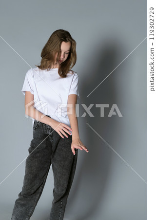 A girl stands in a relaxed, thoughtful pose, dressed casually in jeans and a white t-shirt. The minimalistic setting highlights the calm and introspective nature of modern youth photography. A girl stands in a relaxed, thoughtful pose, dressed casually in jeans and a white t-shirt. The minimalistic setting highlights the calm and introspective nature of modern youth photography. 119302729