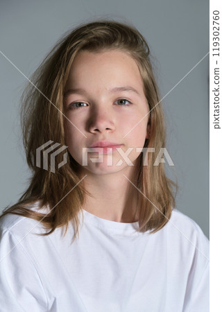 A close-up image of a young girl with a gentle smile, wearing a plain white shirt. The portrait emphasizes her natural beauty and serene demeanor, perfect for themes of youth and simplicity. 119302760