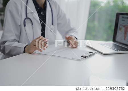 Doctor and a patient are sitting at the white table in clinic. The female physician is using clipboard for making notes during a consultation, close up of woman hands. Medicine concept Doctor and a patient are sitting at the white table in clinic. The female physician is using clipboard for making notes during a consultation, close up of woman hands. Medicine concept 119302762