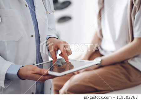 Doctor and patient in clinic. Friendly physician using tablet computer near a young woman. Medicine concept Doctor and patient in clinic. Friendly physician using tablet computer near a young woman. Medicine concept 119302768