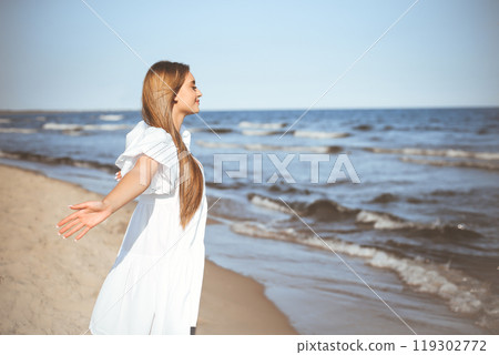 Happy, beautiful woman on the ocean beach standing in a white summer dress, open arms Happy, beautiful woman on the ocean beach standing in a white summer dress, open arms 119302772