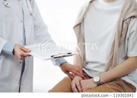 Doctor and patient in clinic. Friendly physician examining a young woman with a one hand while keeping a clipboard with medical records in another. Medicine concept 119302841
