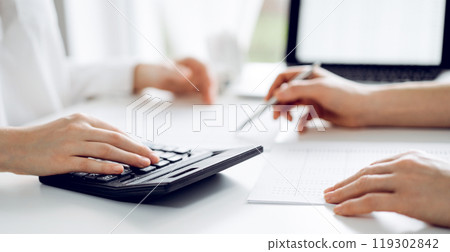 Two accountants using a laptop computer and calculator for counting taxes at white desk in office. Teamwork in business audit and finance 119302842