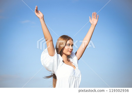 Happy, beautiful woman on the ocean beach standing in a white summer dress, raising hands Happy, beautiful woman on the ocean beach standing in a white summer dress, raising hands 119302936