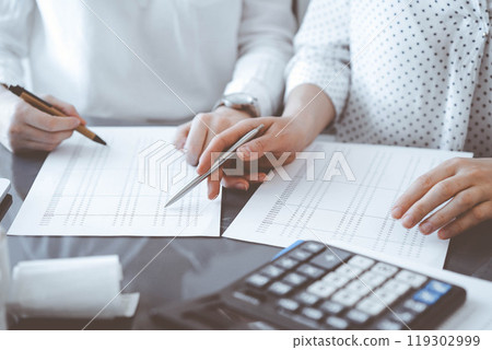 Two accountants use a calculator and laptop computer for counting taxes or revenue balance. Business, audit, and taxes concepts Two accountants use a calculator and laptop computer for counting taxes or revenue balance. Business, audit, and taxes concepts 119302999