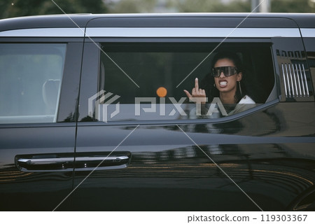 Shot through open car window of pissed off Middle Eastern female celebrity showing middle finger to paparazzi while wearing trendy sunglasses sitting in backseat of limo, copy space 119303367