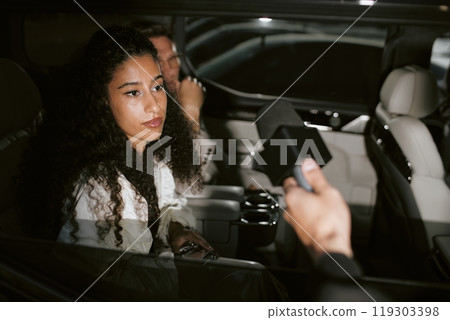Medium shot of Middle Eastern female celebrity sitting in back seat of car in camera light interviewed by television correspondents through open window, camera flash, copy space 119303398