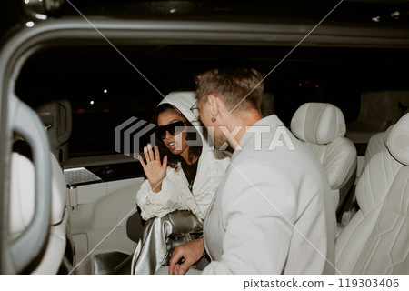 Middle Eastern female celebrity in sunglasses hiding with hand from photographers caught by paparazzi with man sitting in limo back seat, privacy invasion, copy space 119303406