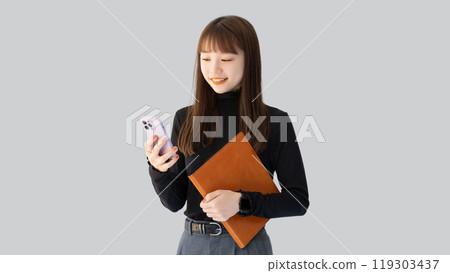 Smiling woman/businesswoman holding a smartphone and a binder 119303437