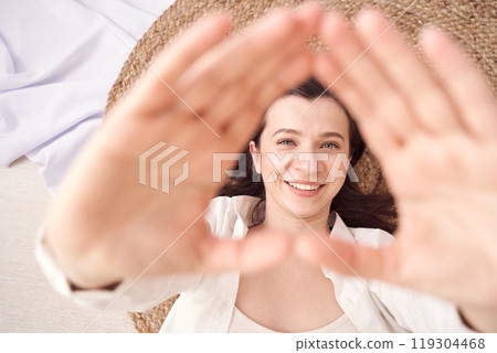 Woman lying down smiling with hands framing face in natural light setting 119304468