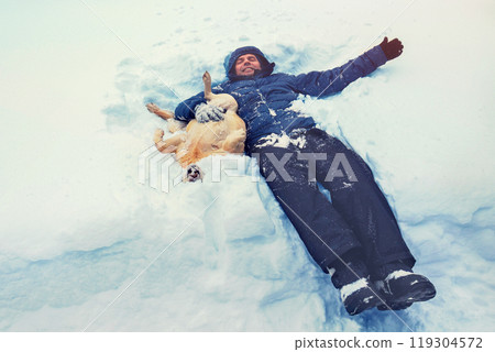 Happy smiling man with labrador retriever dog lying on the snow 119304572