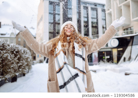 Smiling woman in a scarf and hat is having fun at street holiday fair, drinking hot drink. 119304586