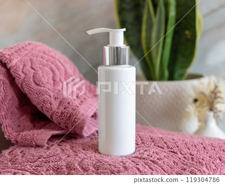 White cosmetic pump bottle on pink towels near green plant close up in bathroom, mockup 119304786