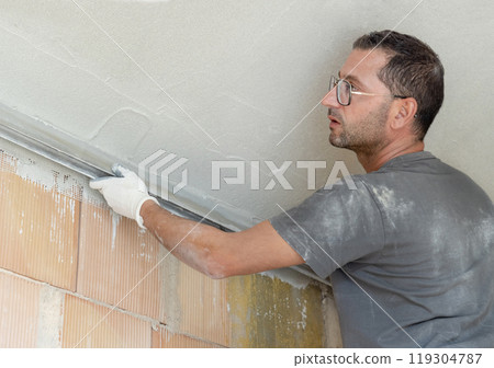 Craftsman in dirty gloves and gray shirt checking the ceiling surface with straight edge 119304787
