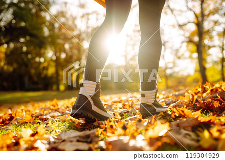Close-up of feet in hiking boots in clearing among fallen leaves in sunny autumn park. outdoor walk. Close-up of feet in hiking boots in clearing among fallen leaves in sunny autumn park. outdoor walk. 119304929