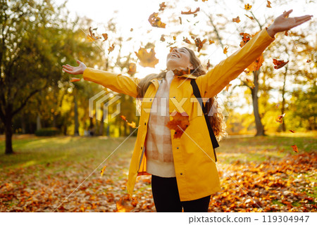 A smiling tourist in a bright coat walks through an autumn park in sunny weather. Travel concept. 119304947