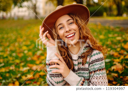 Happy woman in stylish sweater and hat outdoors in autumn park on plaid. Woman enjoys autumn nature. 119304997