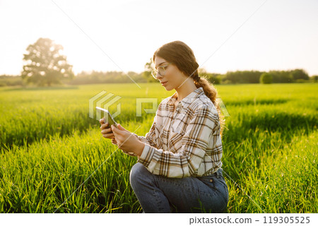 A woman farmer with modern tablet evaluates the shoots with her hand. Farm work with digital tablet. A woman farmer with modern tablet evaluates the shoots with her hand. Farm work with digital tablet. 119305525