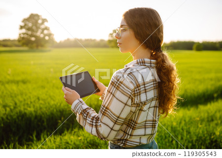 A woman farmer with modern tablet evaluates the shoots with her hand. Farm work with digital tablet. A woman farmer with modern tablet evaluates the shoots with her hand. Farm work with digital tablet. 119305543