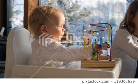 Baby girl plays with an educational toy in a warm cafe, surrounded by her loving family on a beautiful winter day Baby girl plays with an educational toy in a warm cafe, surrounded by her loving family on a beautiful winter day 119305659