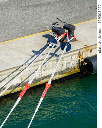 A tense stretched ship's thick mooring rope at the mooring bollard of the harbor quay, ship securing A tense stretched ship's thick mooring rope at the mooring bollard of the harbor quay, ship securing 119305952