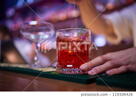 Bartender pours pink cocktail into martini glass with flair 119306426