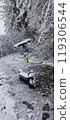 A colorful scooter covered in snow rests on a winter path surrounded by snow-laden trees in a tranquil snowfall setting 119306544