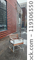 A wooden chair covered in snow beside a modern building on a chilly winter day in an urban neighborhood 119306550